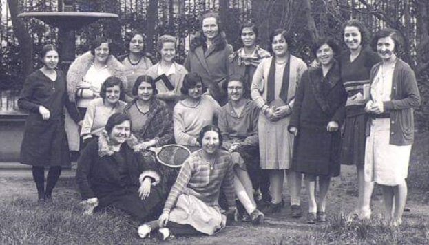 Black and white photograph of a group of students and teachers posing and smiling in the garden of the Residencia de Señoritas, some holding tennis rackets